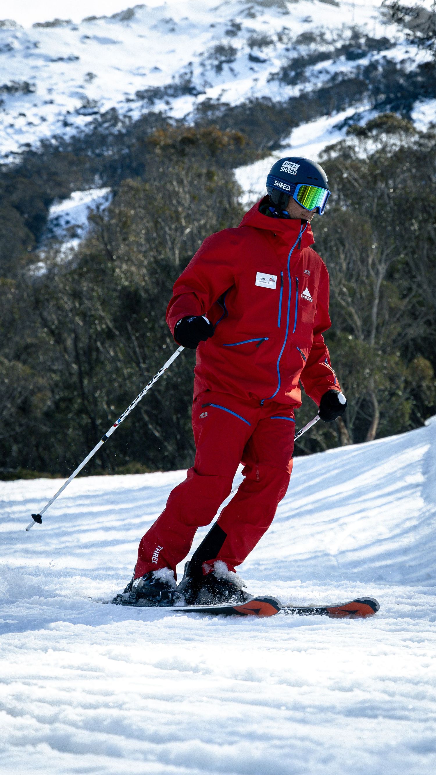 Skier in red jacket and pants skiing down a snowy mountain slope wearing a black helmet and goggles.