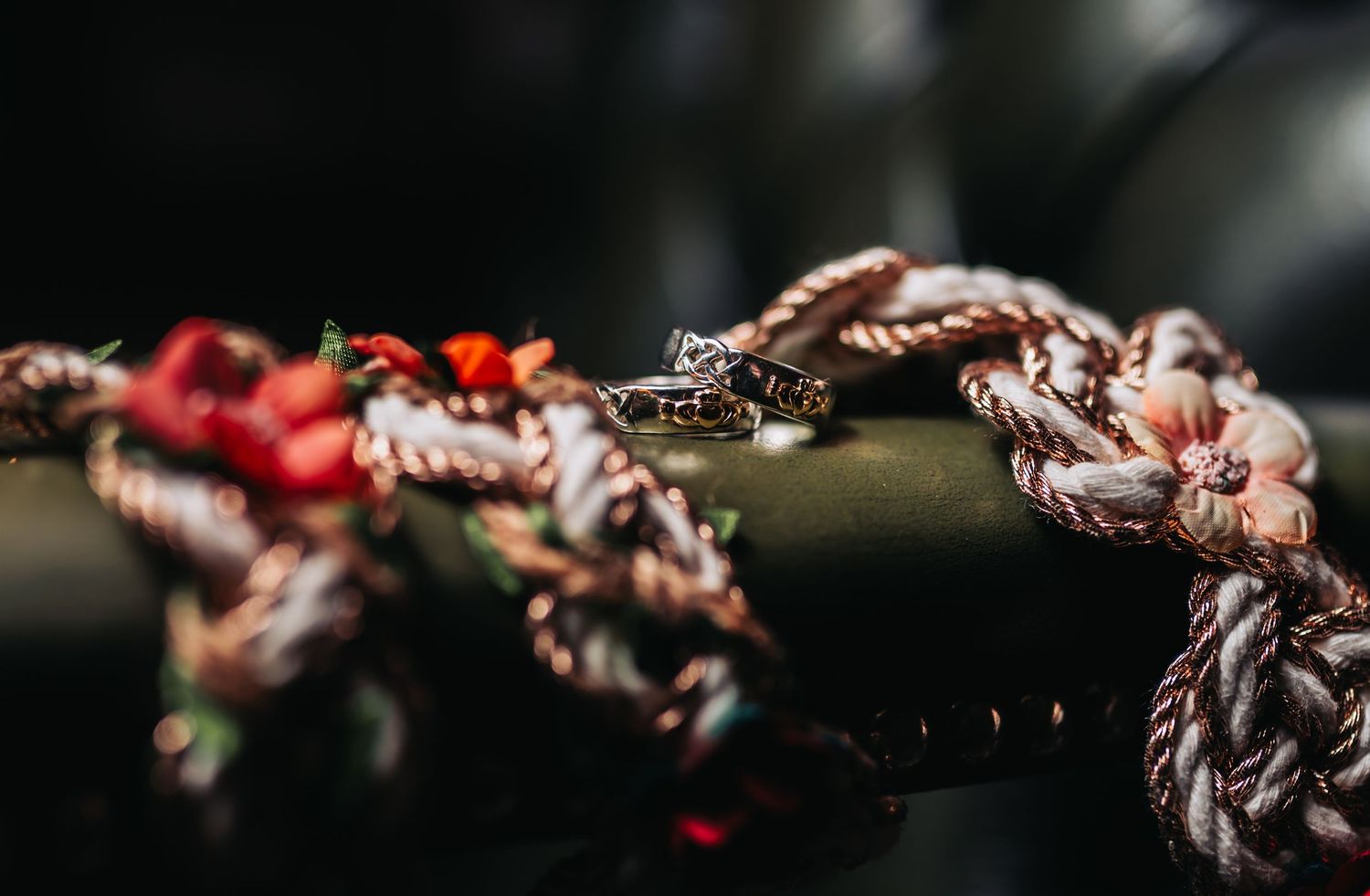 Colorful braided rope bracelets with a small ring displayed on a dark wooden branch.