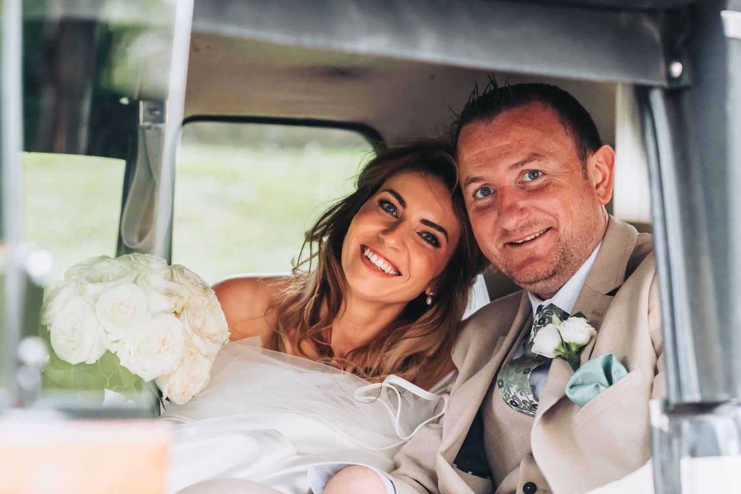 Happy bride and groom smiling together inside a vintage wedding car on their special day.
