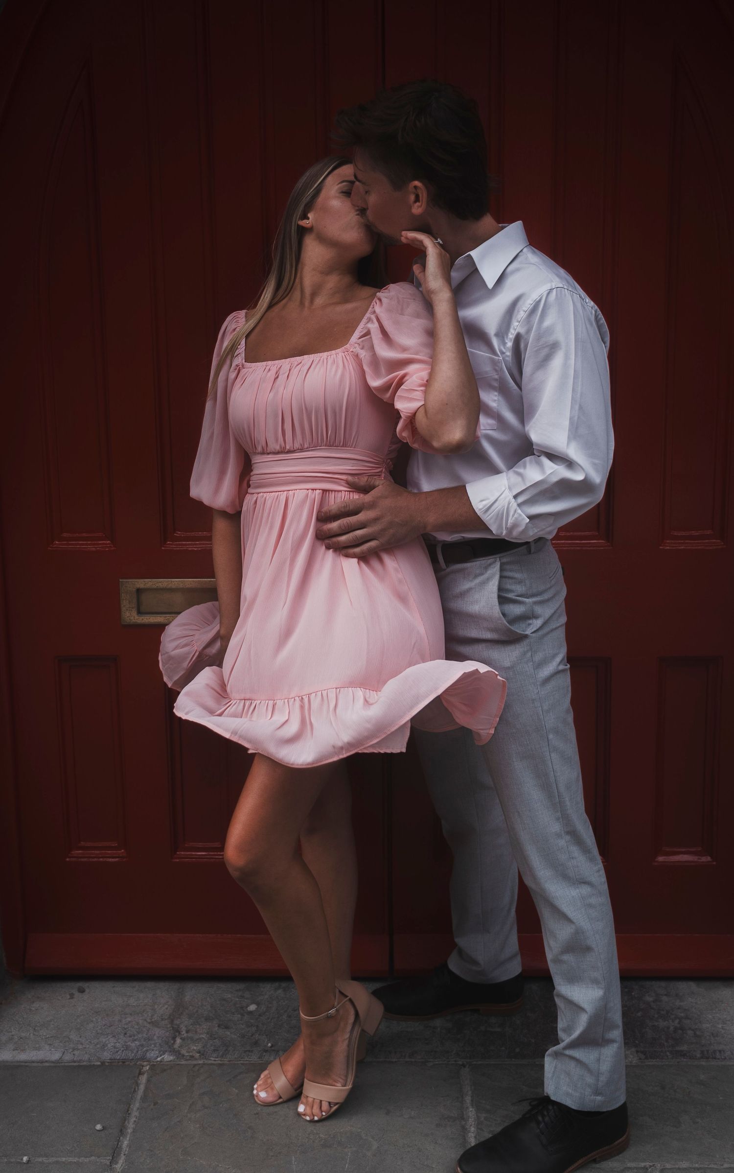 A romantic couple embraces against a red door in an intimate moment.