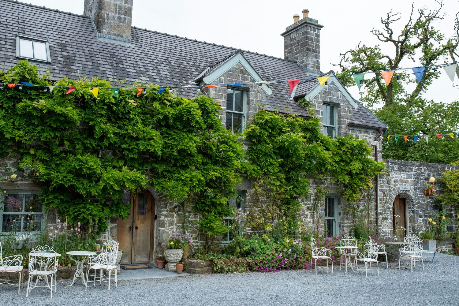 Stone building exterior with white outdoor furniture and flowering plants along the facade.