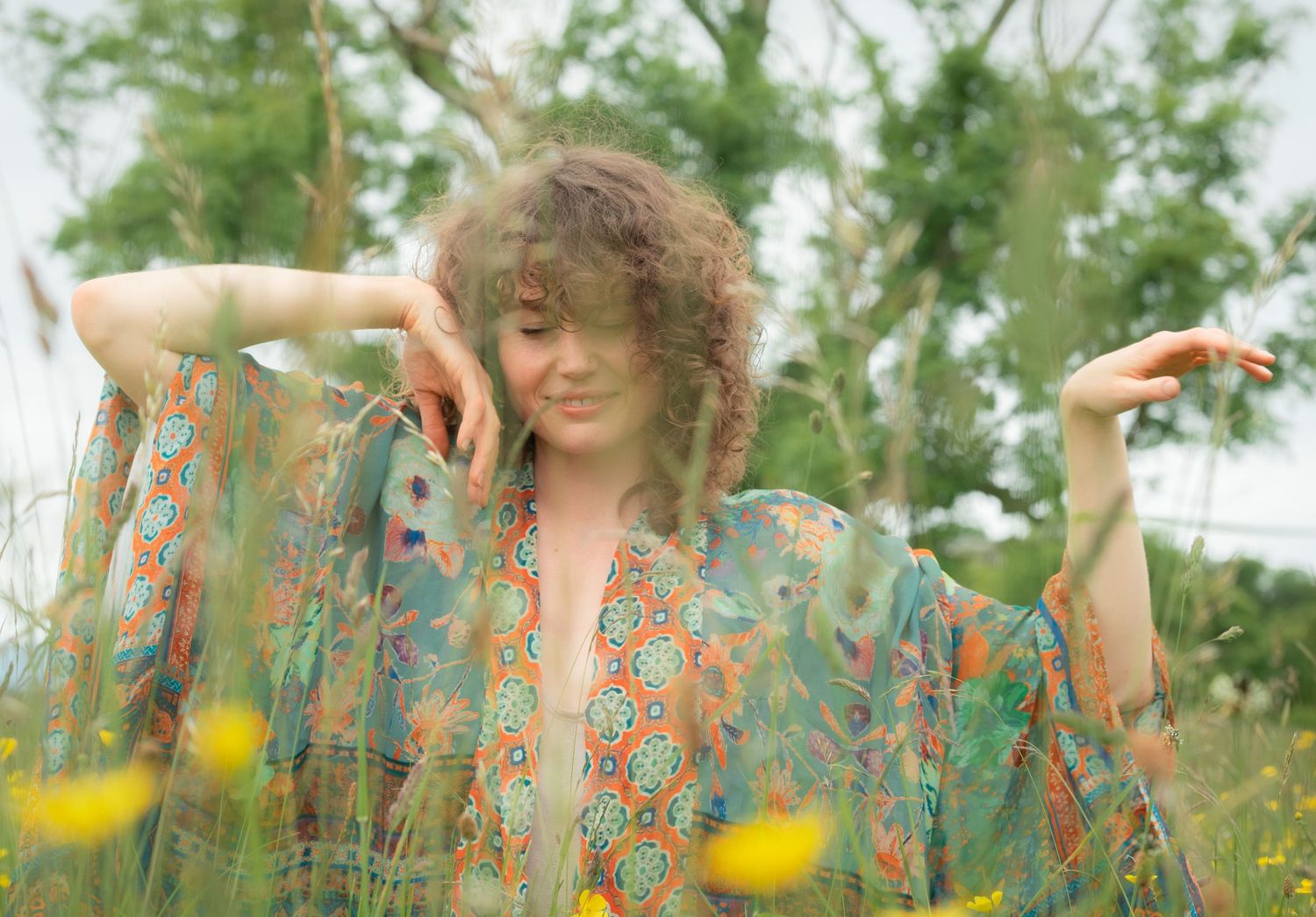Young woman with curly hair wearing a floral kimono posing in a field of wildflowers.