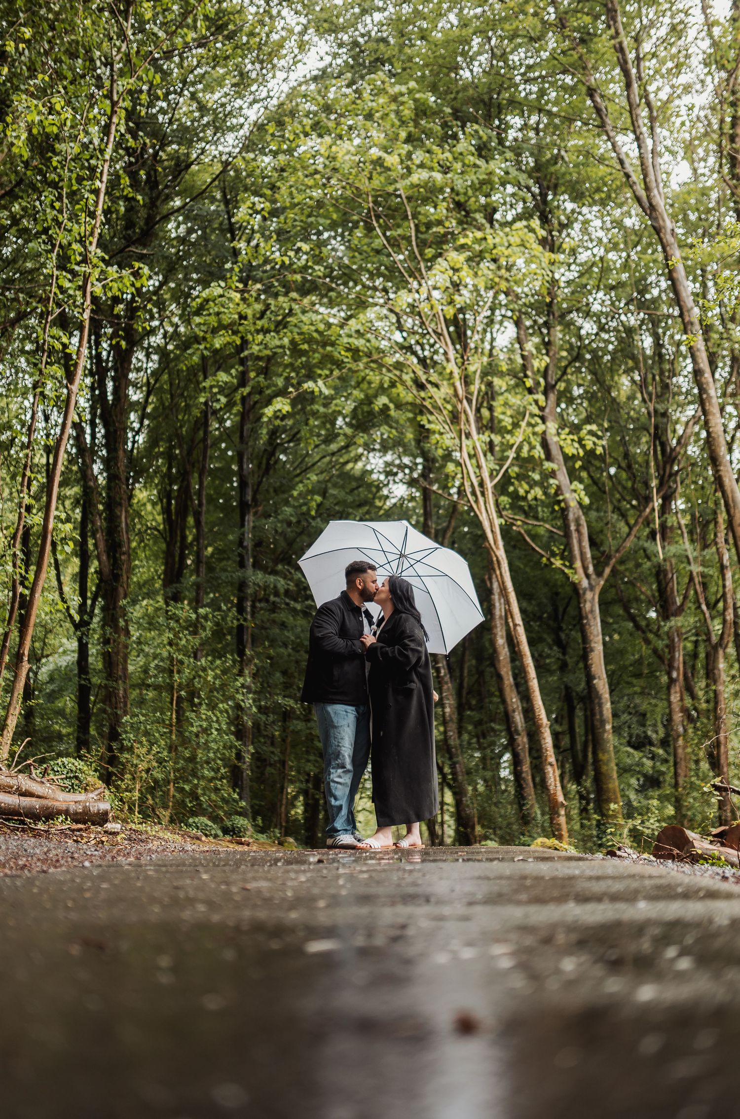 Couple with umbrella walking through wooded area on rainy day.