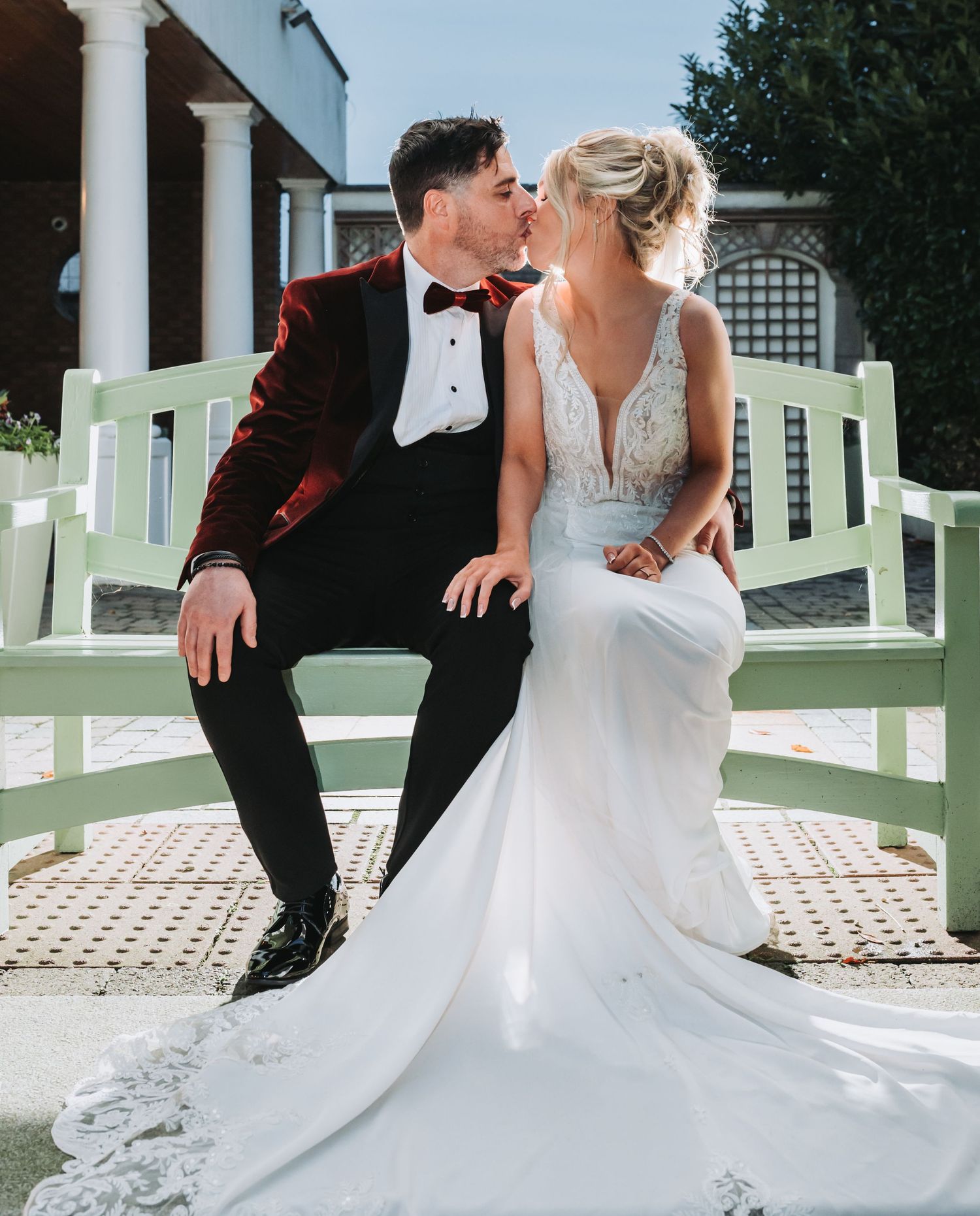 Wedding couple poses playfully on a white porch with classic architectural details.