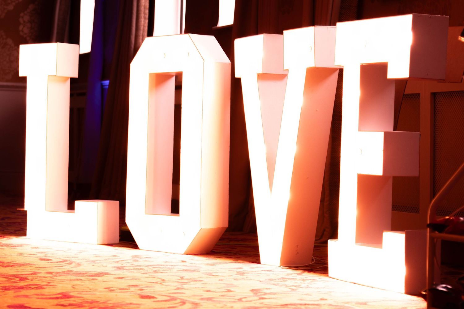 Large illuminated LOVE letters display glowing warmly at a wedding reception venue event.