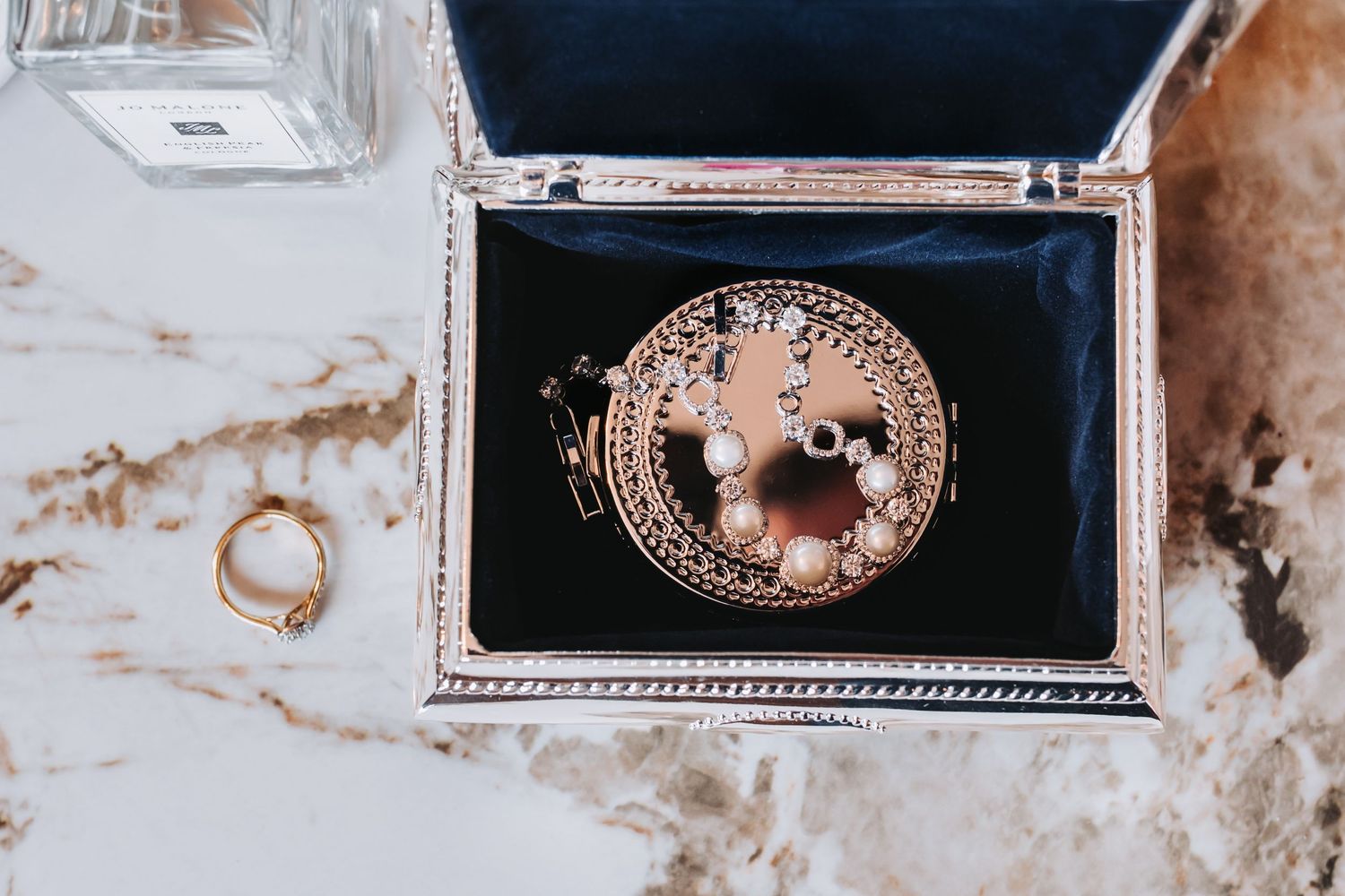 Elegant wedding jewelry box with pearl earrings and gold ring on marble surface.