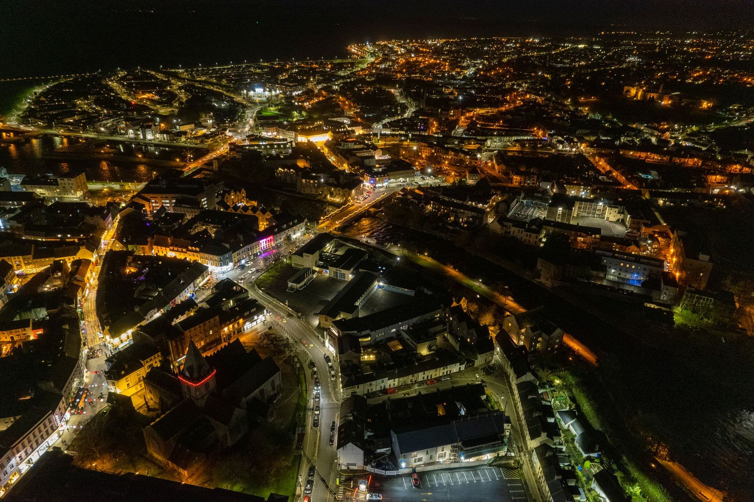 Aerial night view of a glowing European city with illuminated streets and buildings stretching to the horizon.