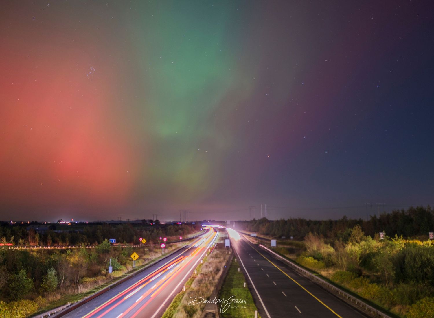 Stunning aurora borealis with red and green lights over a highway with car light trails at night.