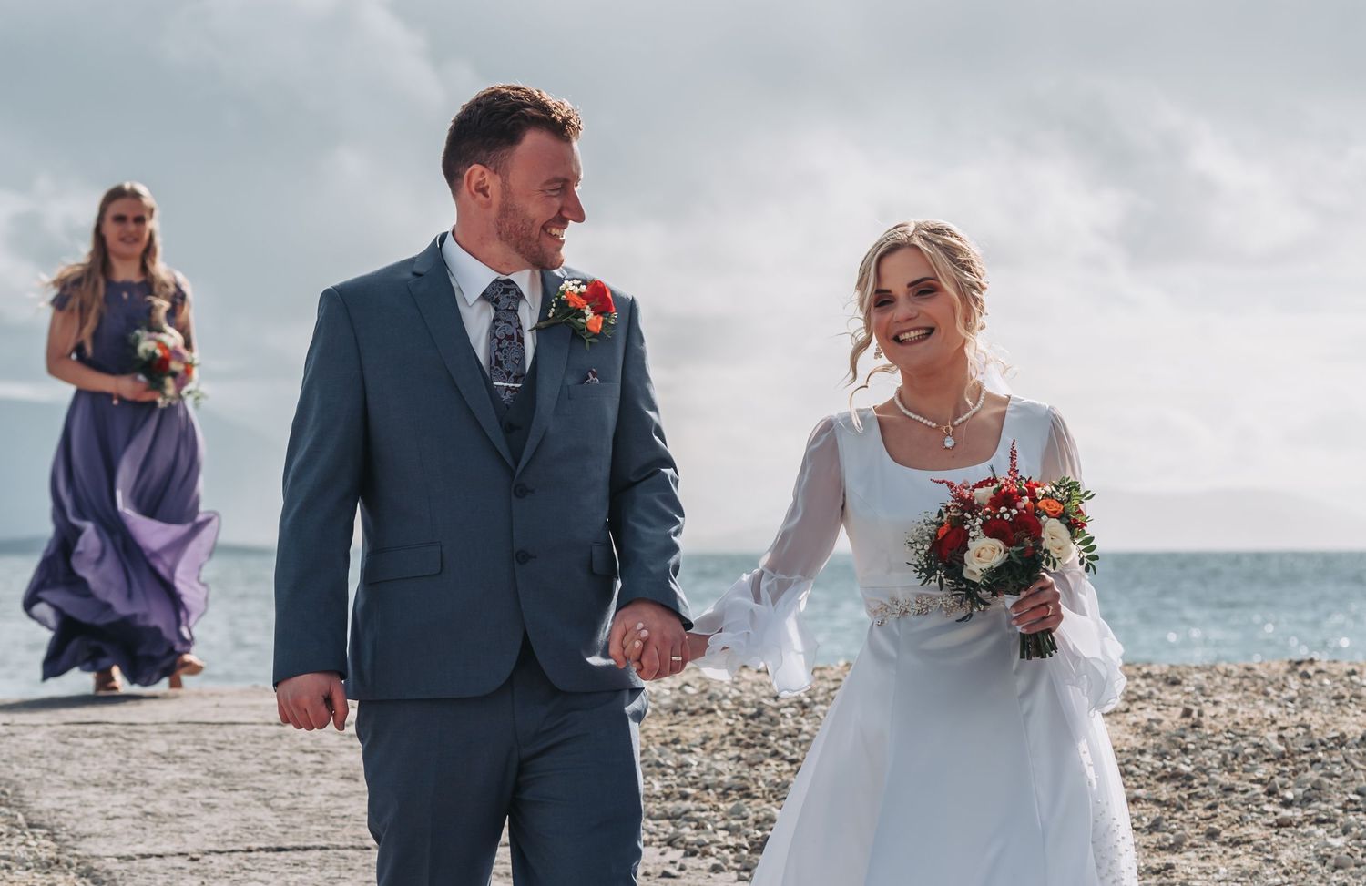 Couple walks along a rocky beach shoreline on their wedding day.