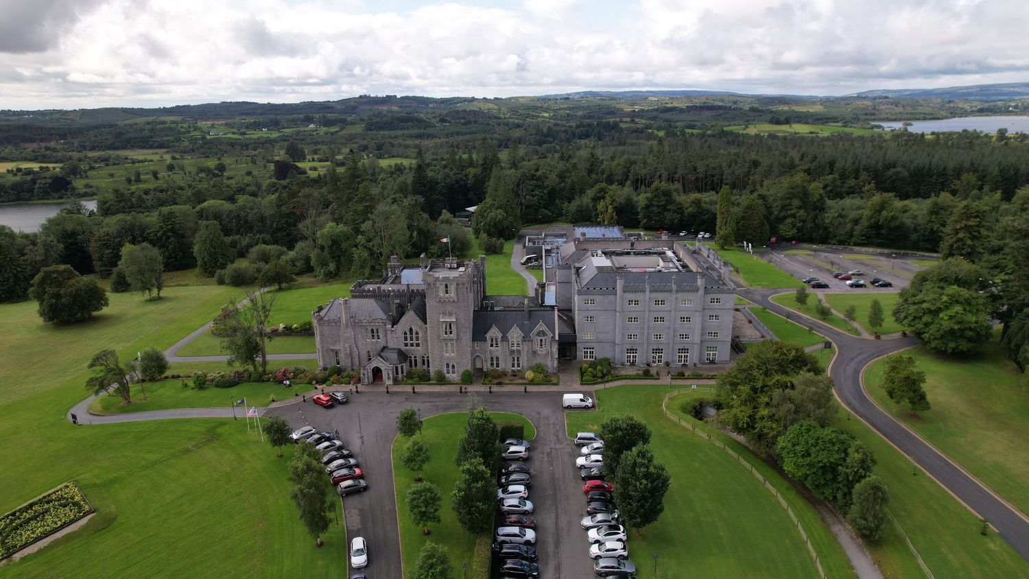Aerial view of grand castle hotel with parking area surrounded by lush green landscape.