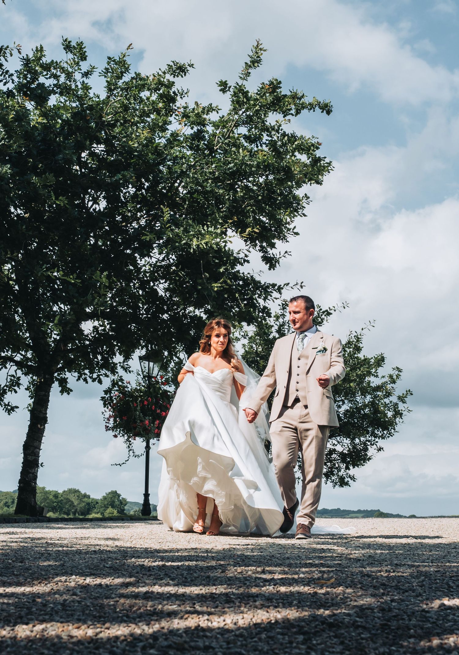 Wedding couple relaxing on a grassy hill under trees on a sunny day.