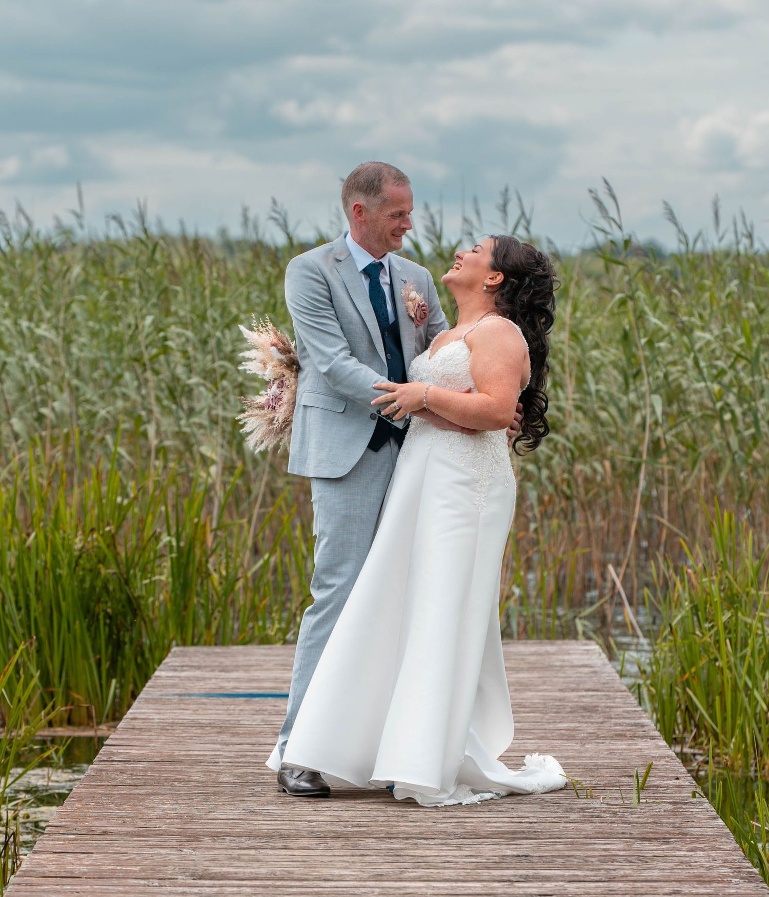 Couple dances on wooden boardwalk surrounded by marsh grass during wedding celebration.