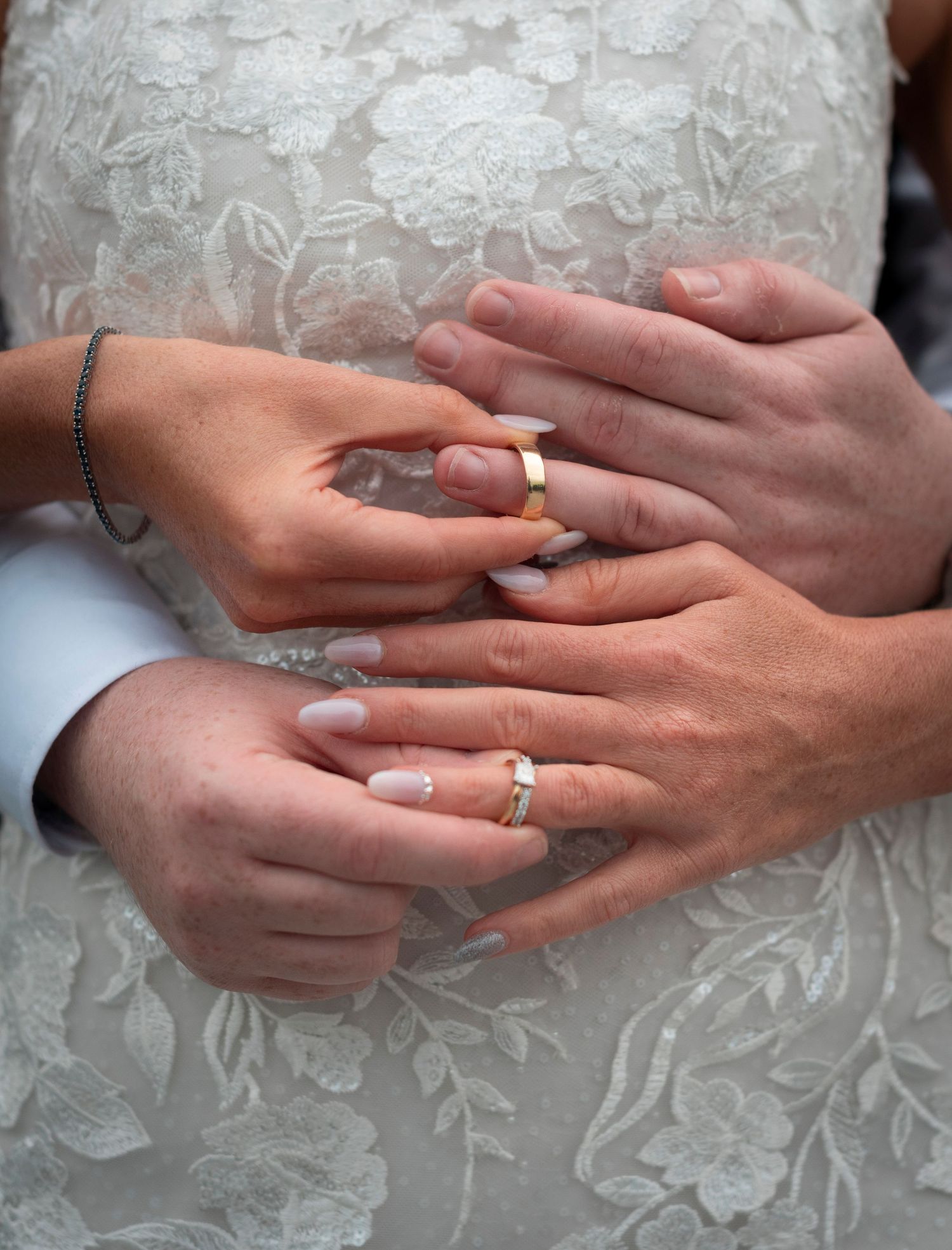 Close-up of hands displaying wedding rings against intricate lace fabric.