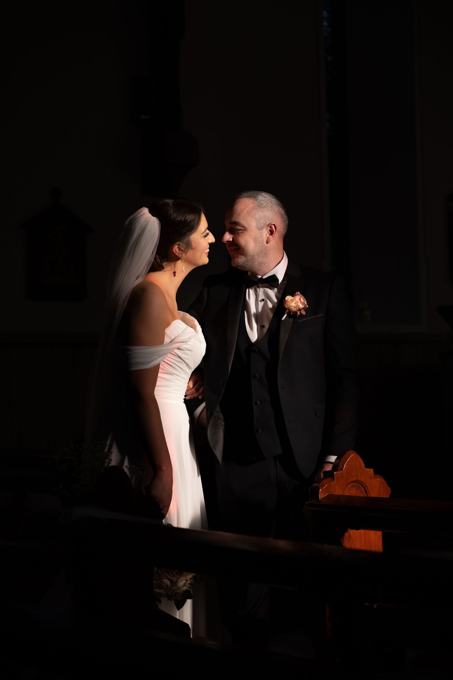 Dramatic lighting captures intimate moment in formal attire against dark background.