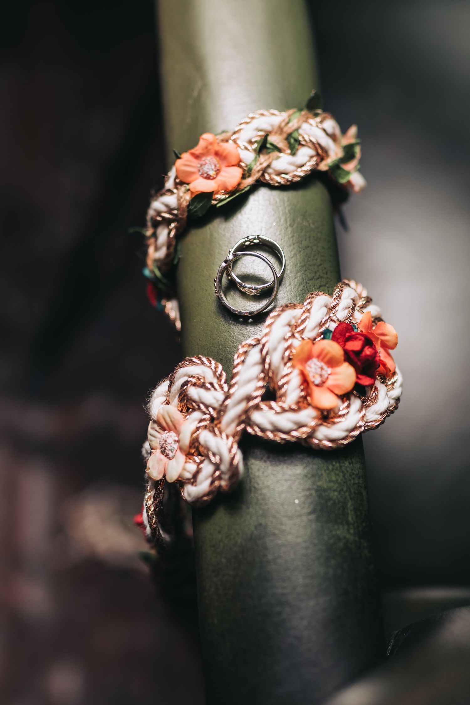 Two wedding rings resting on a decorative rope bracelet with orange flowers on a green bamboo stem.