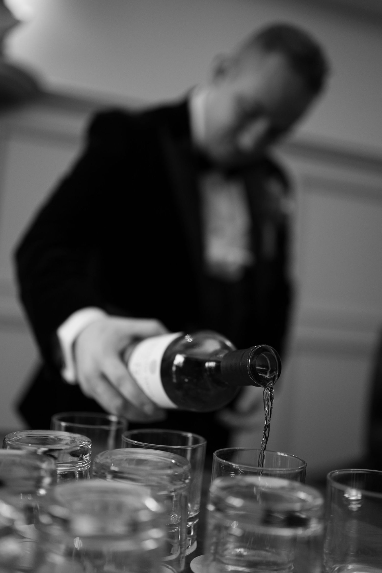 Bartender pouring wine into glasses at a wedding reception in black and white.