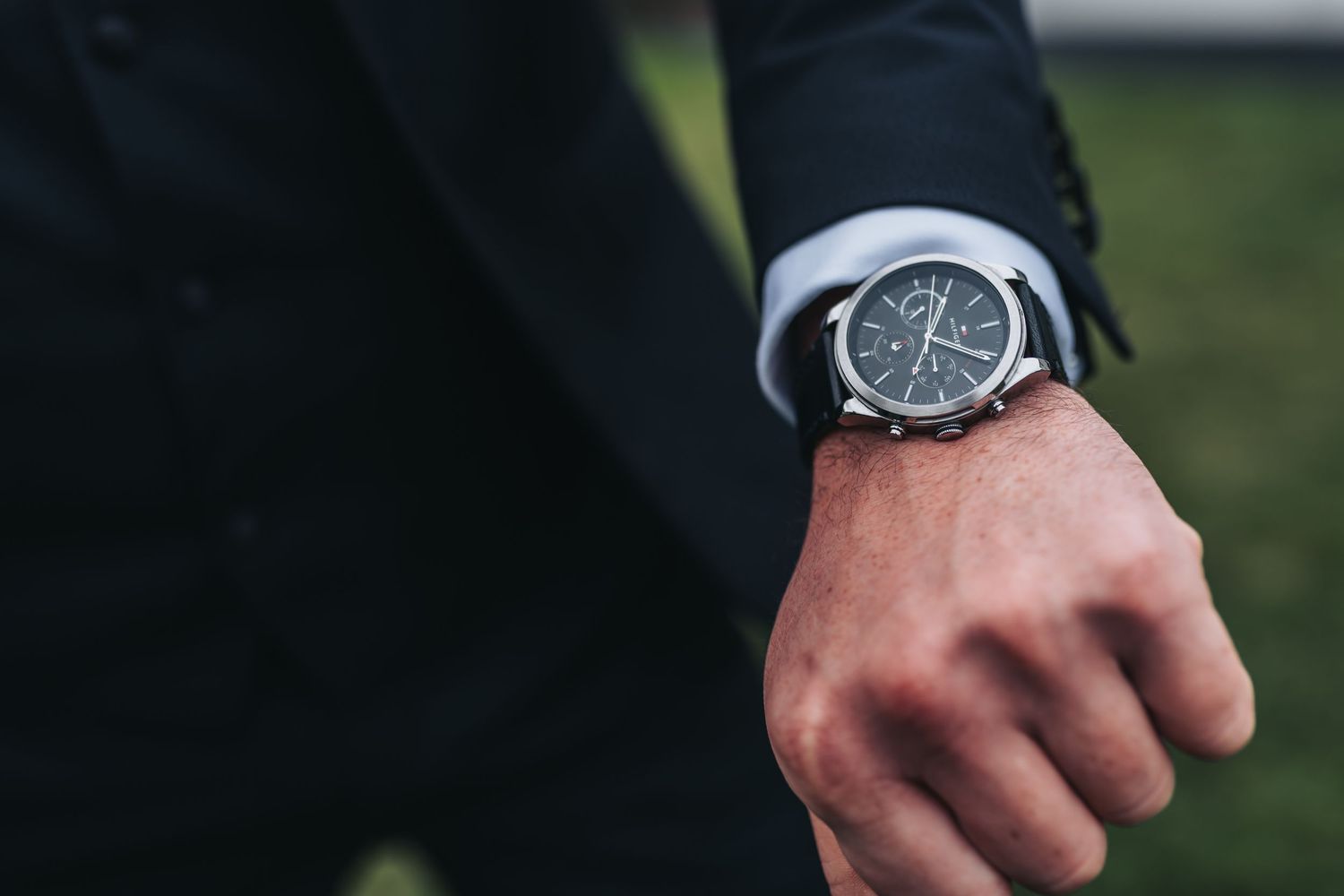 Man in black suit checking time on a classic black chronograph wristwatch with silver case.