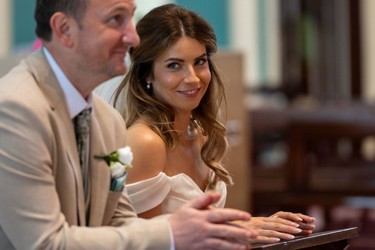 Smiling bride in off-shoulder gown seated beside groom during wedding ceremony.