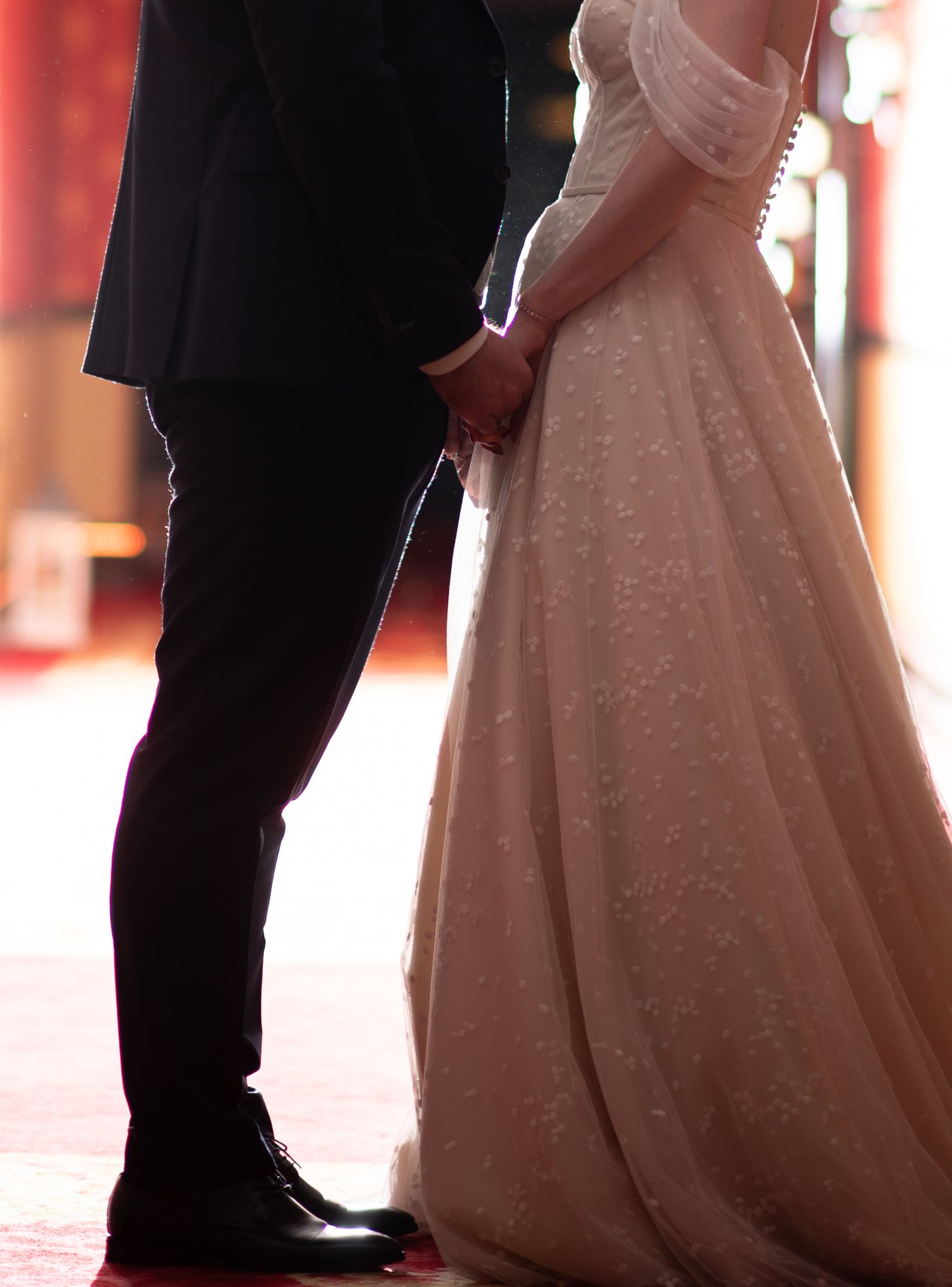 Bride and groom hold hands during wedding ceremony, bride wearing an elegant lace off-shoulder ballgown.