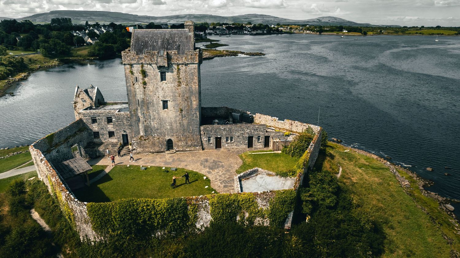 Panoramic view of historic castle on coastline with dramatic cloudy sky.