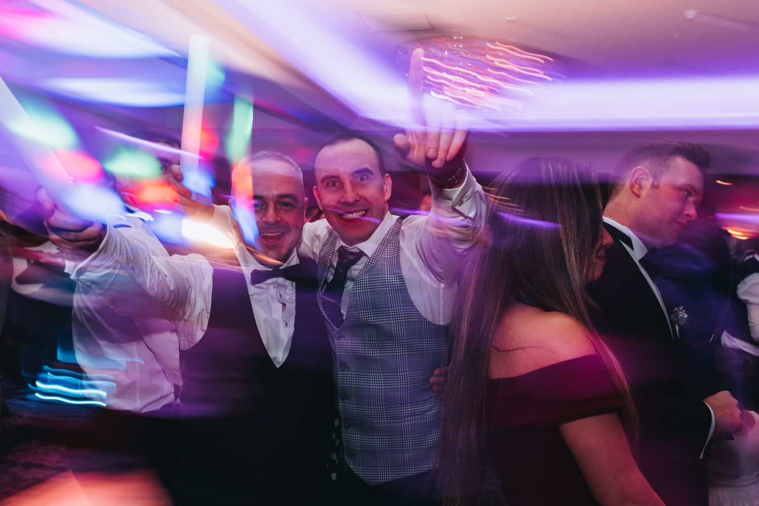 Colorful party lights illuminate a lively wedding reception dance floor.