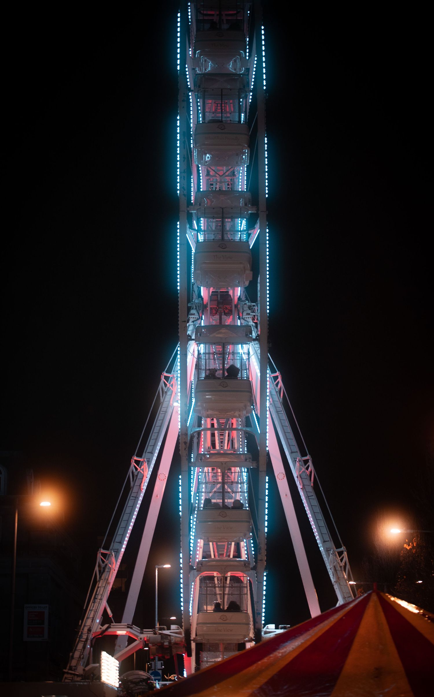 A brightly lit Ferris wheel with blue and red LED lights stands tall against a dark night sky at a fair.