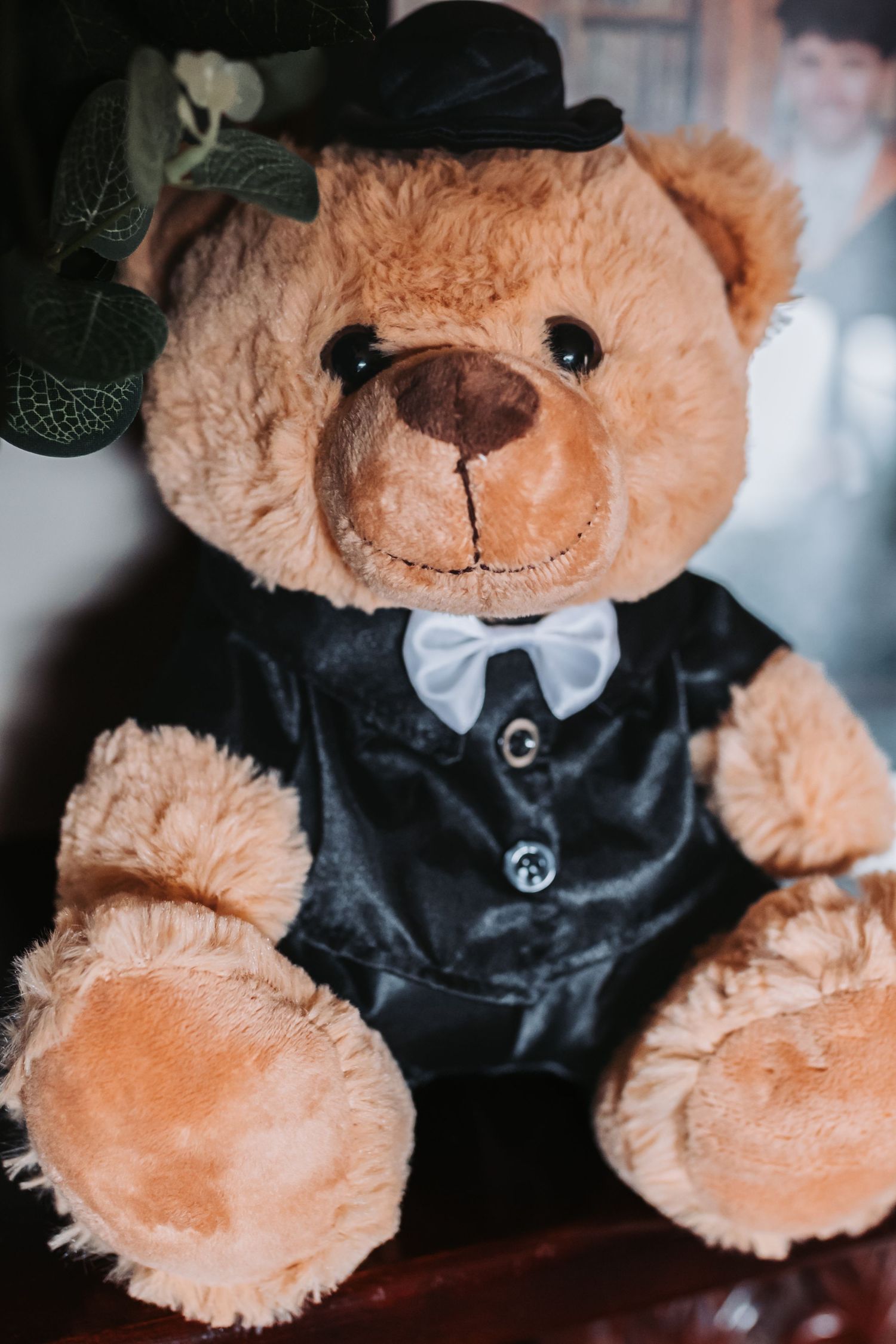 Cute brown teddy bear dressed in a black tuxedo suit with white bow tie and top hat.