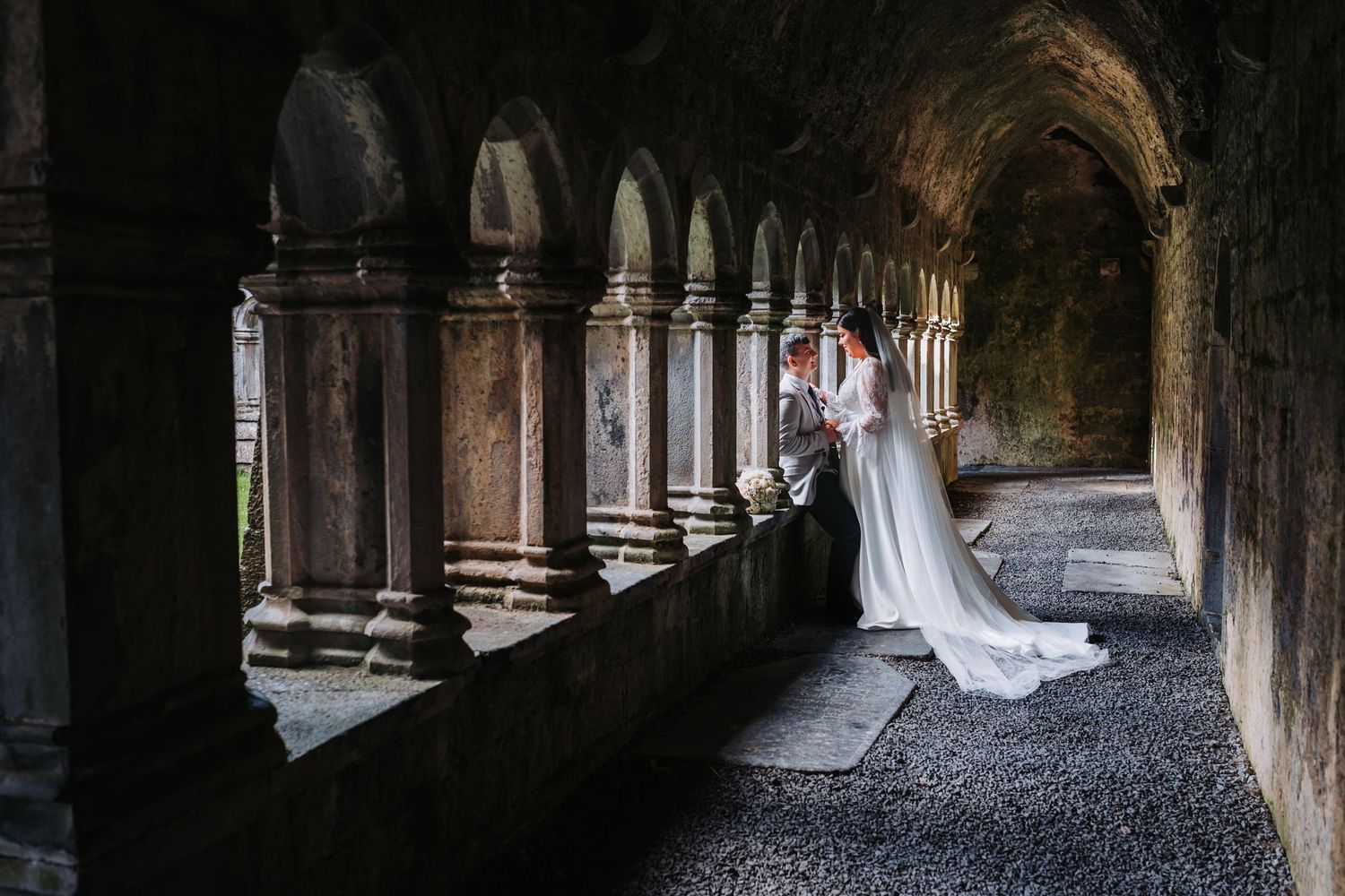 An elegant wedding portrait session in a historic stone cloister with dramatic architectural details.