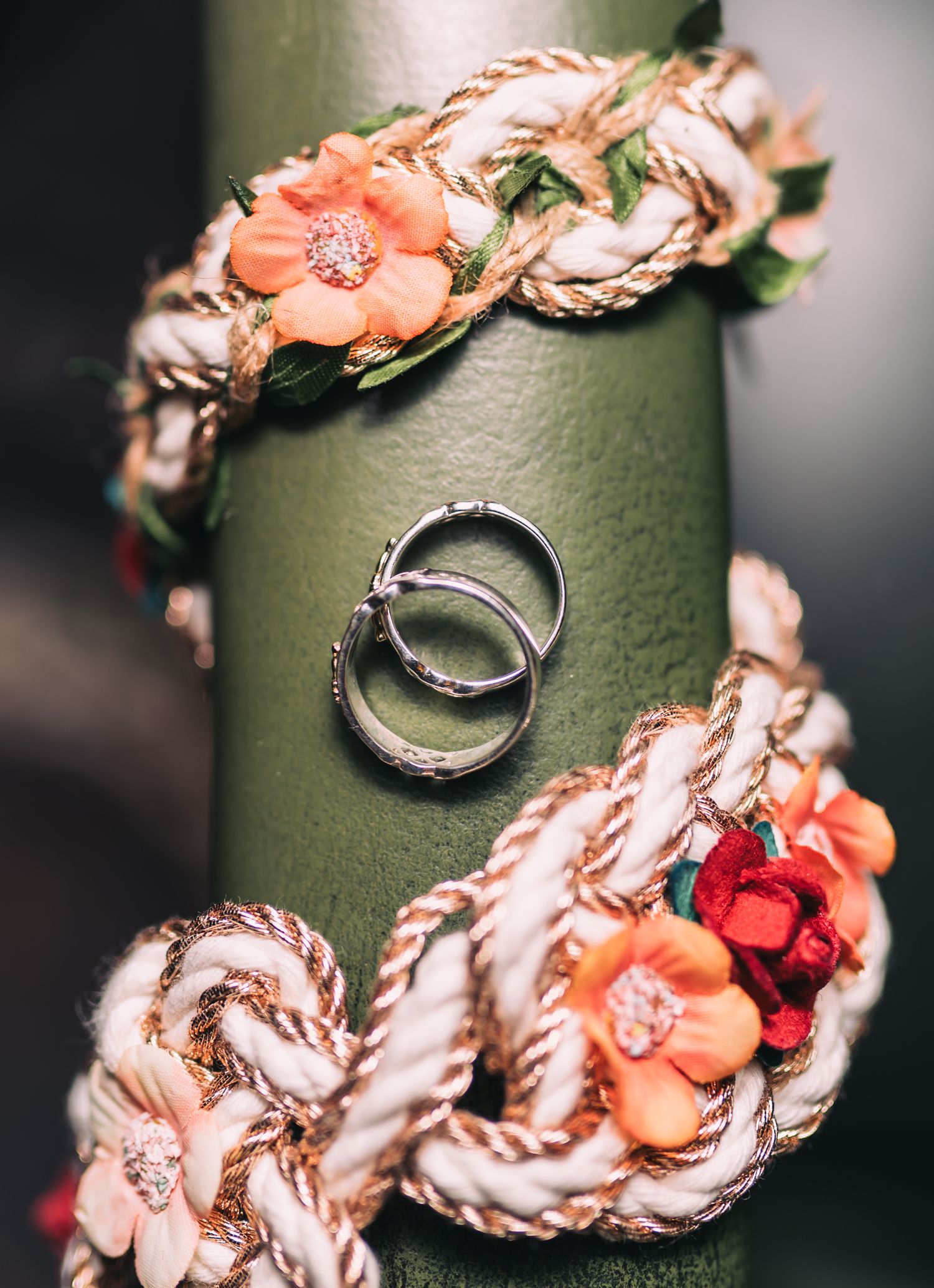 Wedding rings displayed on green surface with coral and peach floral decorative elements.