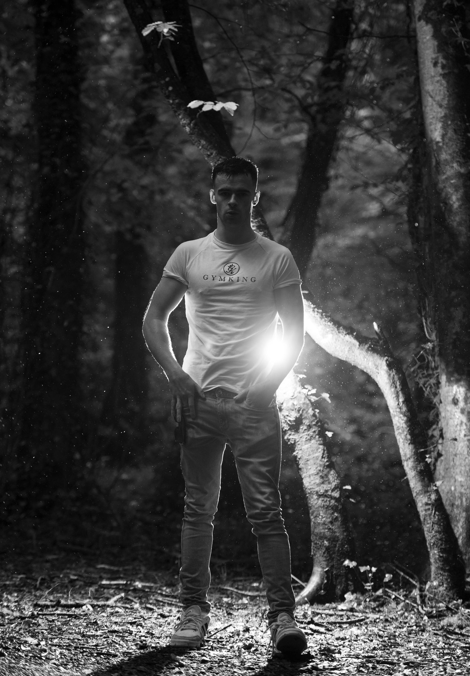 Black and white photo of a man standing in a forest with a bright light flare behind him.