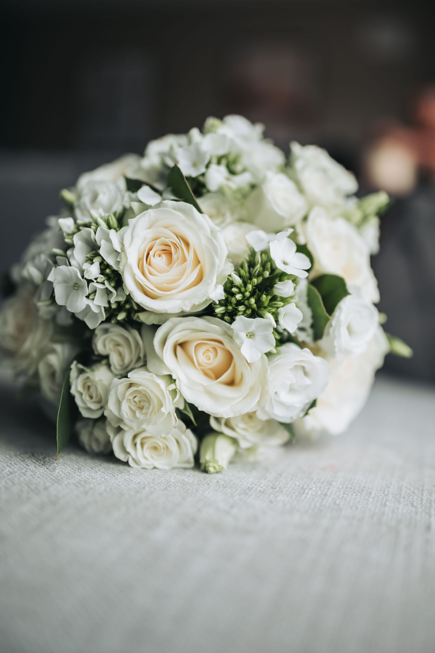 An elegant bridal bouquet of white and cream roses arranged beautifully on a light grey surface.