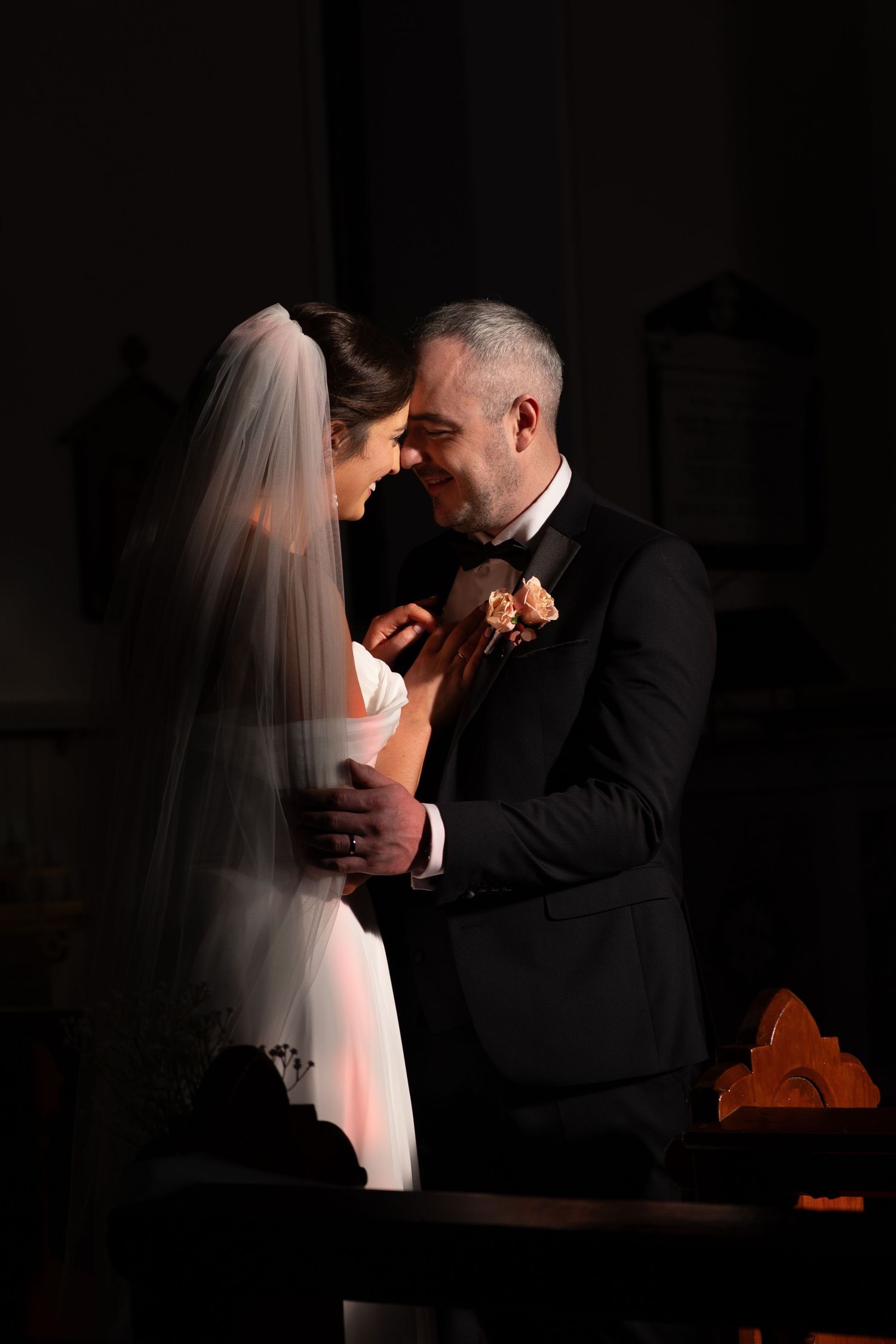 Romantic couple in formal attire sharing an intimate moment in low light.