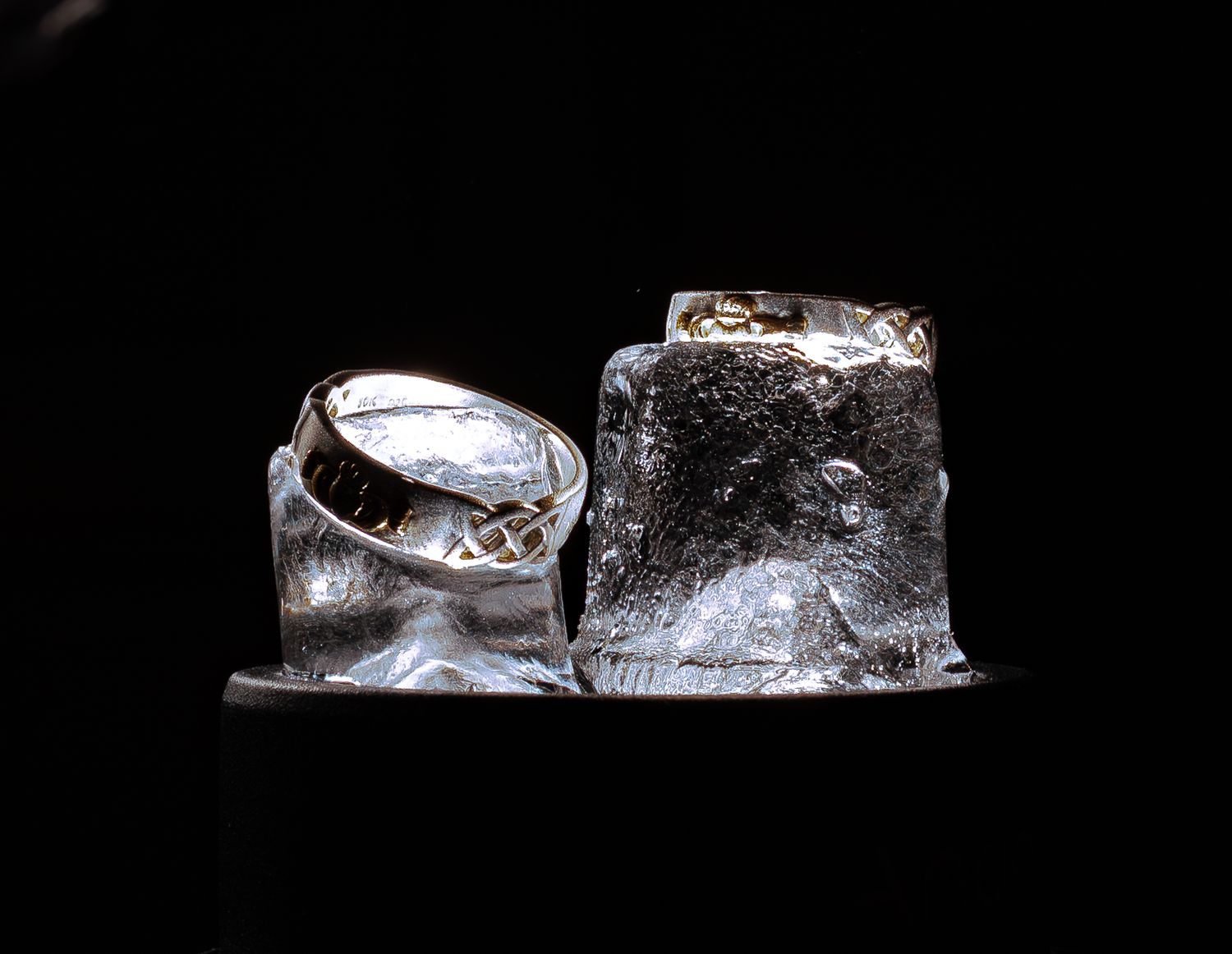 Two clear ice cubes illuminated against black background.