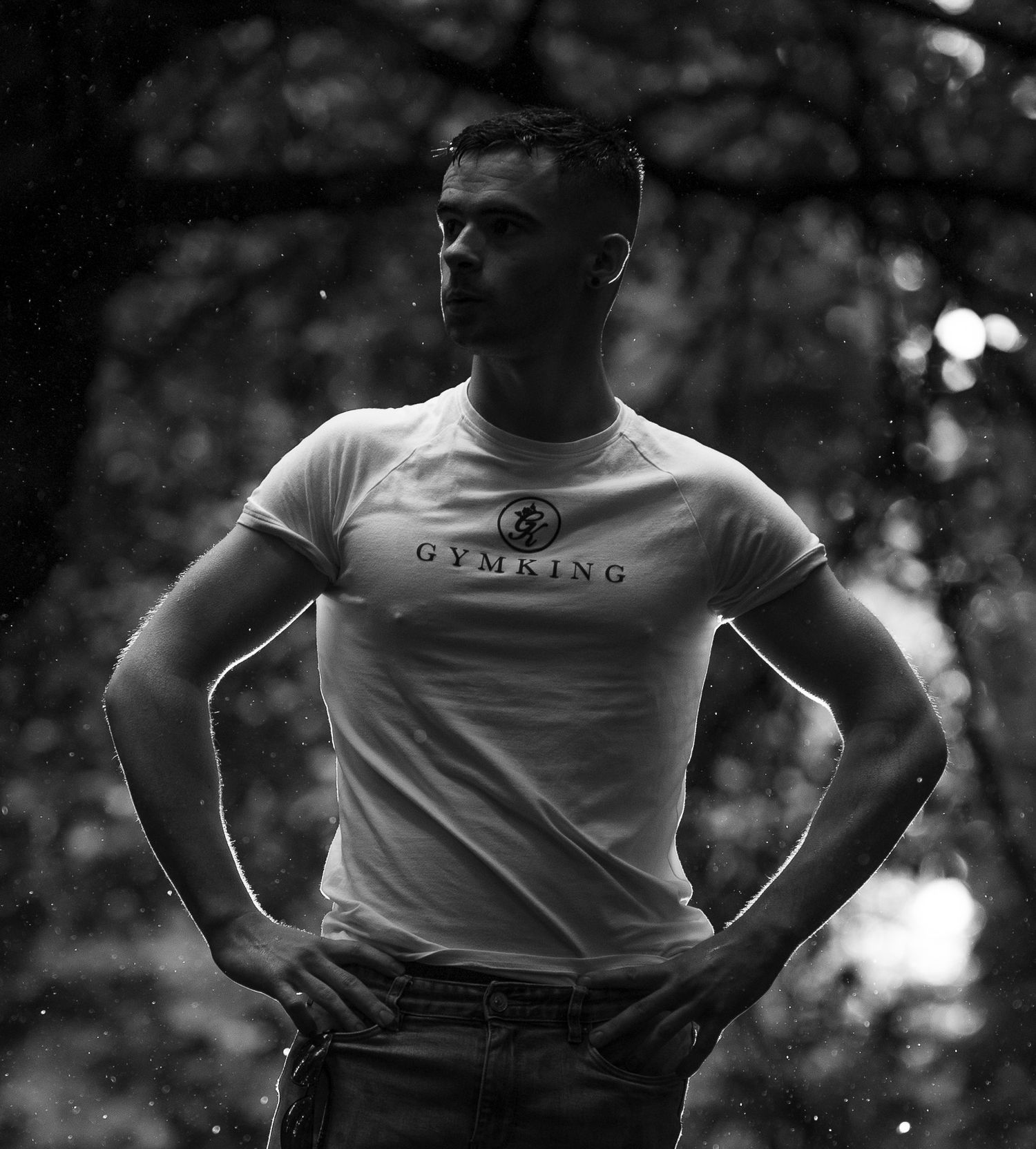 Muscular man in Gymking white t-shirt posing with hands on hips outdoors in black and white photo.