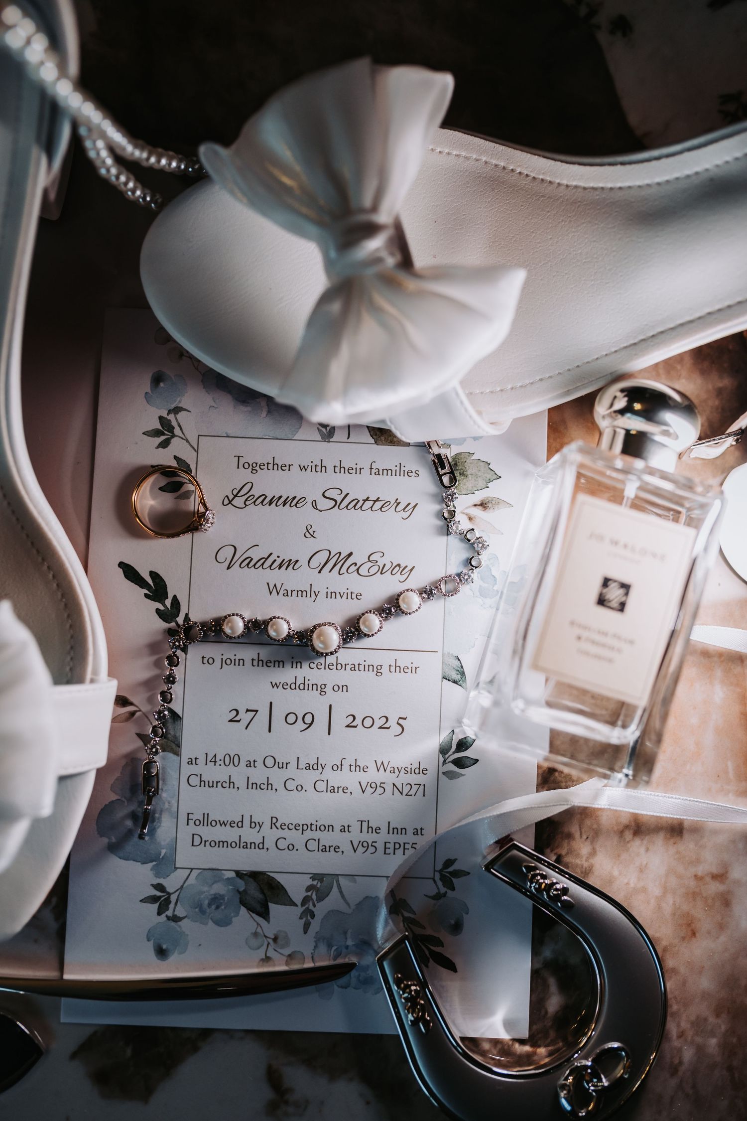 Wedding invitation for Leanne Slattery and Vadim McEvoy, dated 27/09/2025, displayed with bridal shoes, jewelry, and perfume.