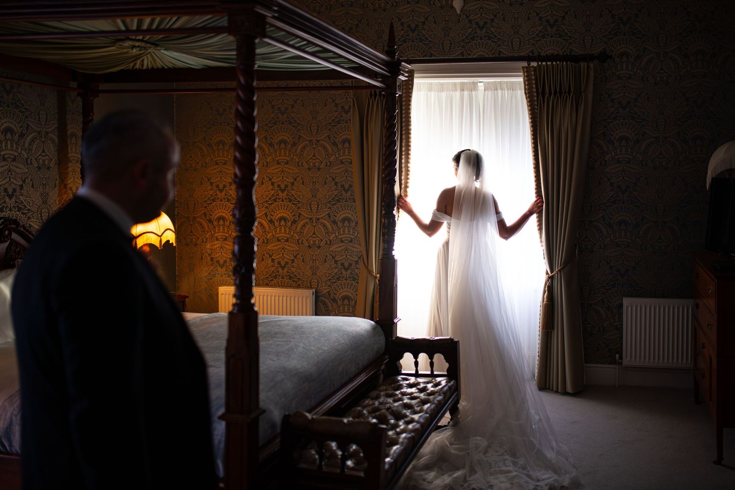 Silhouetted figure stands in dramatic lighting against window creating moody artistic wedding photography.