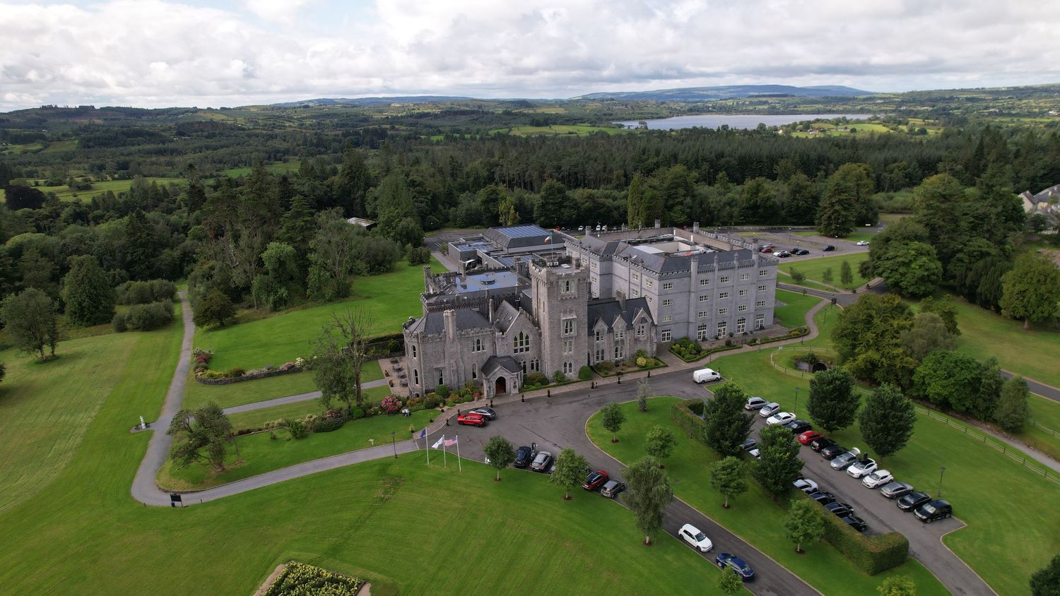 Drone shot of historic stone manor with manicured lawns and lake view in background.