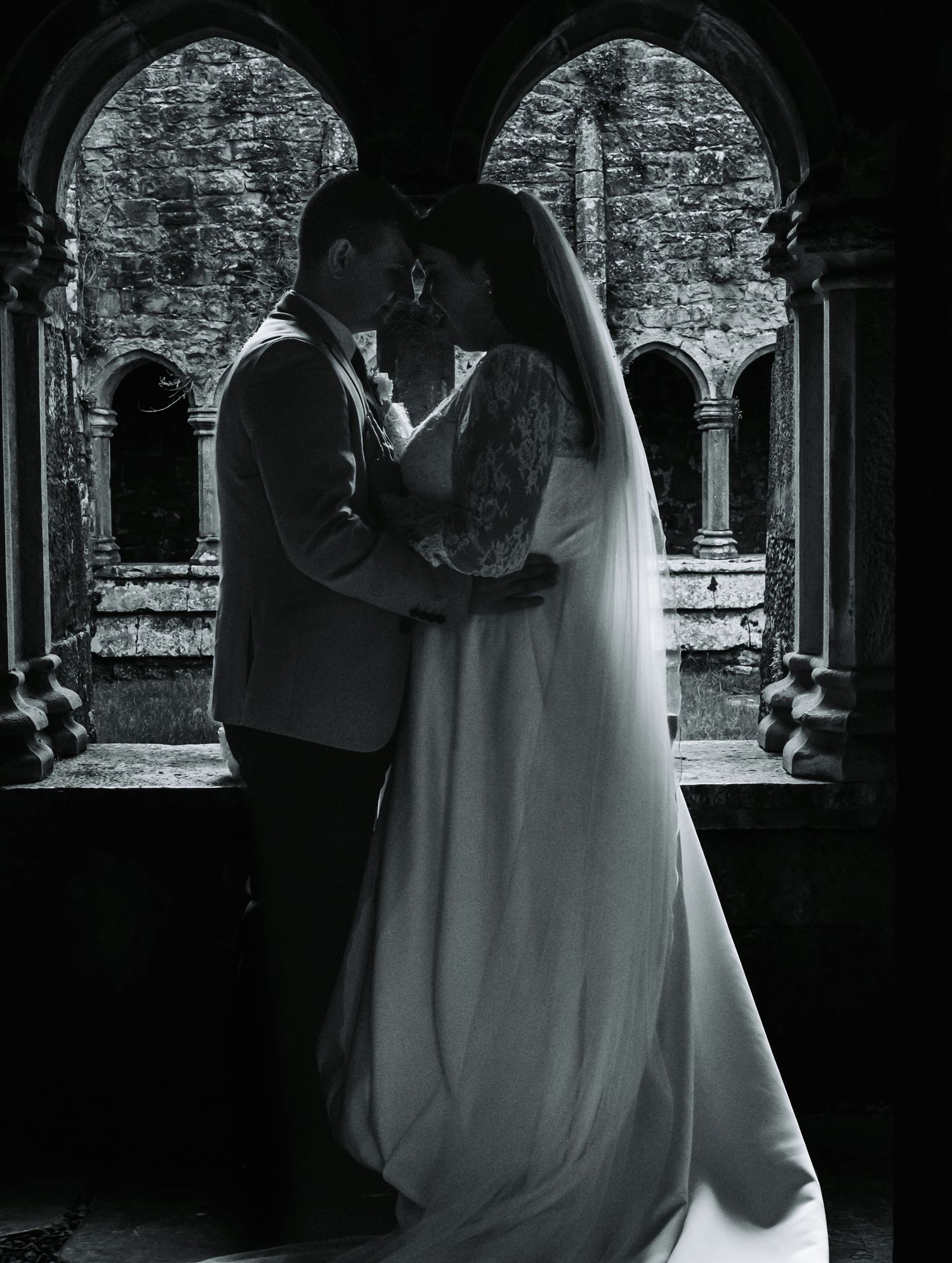 Romantic black and white silhouette of bride and groom embracing in stone archway.