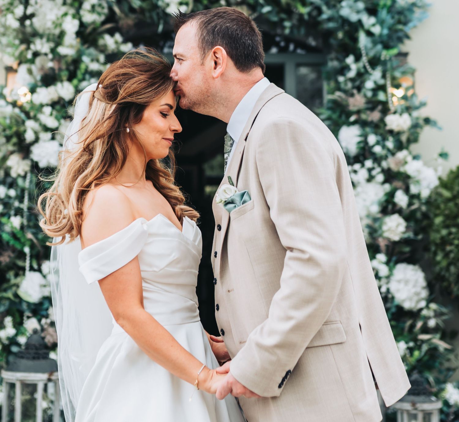 Bride and groom sharing a tender kiss at outdoor wedding ceremony surrounded by white floral decorations.