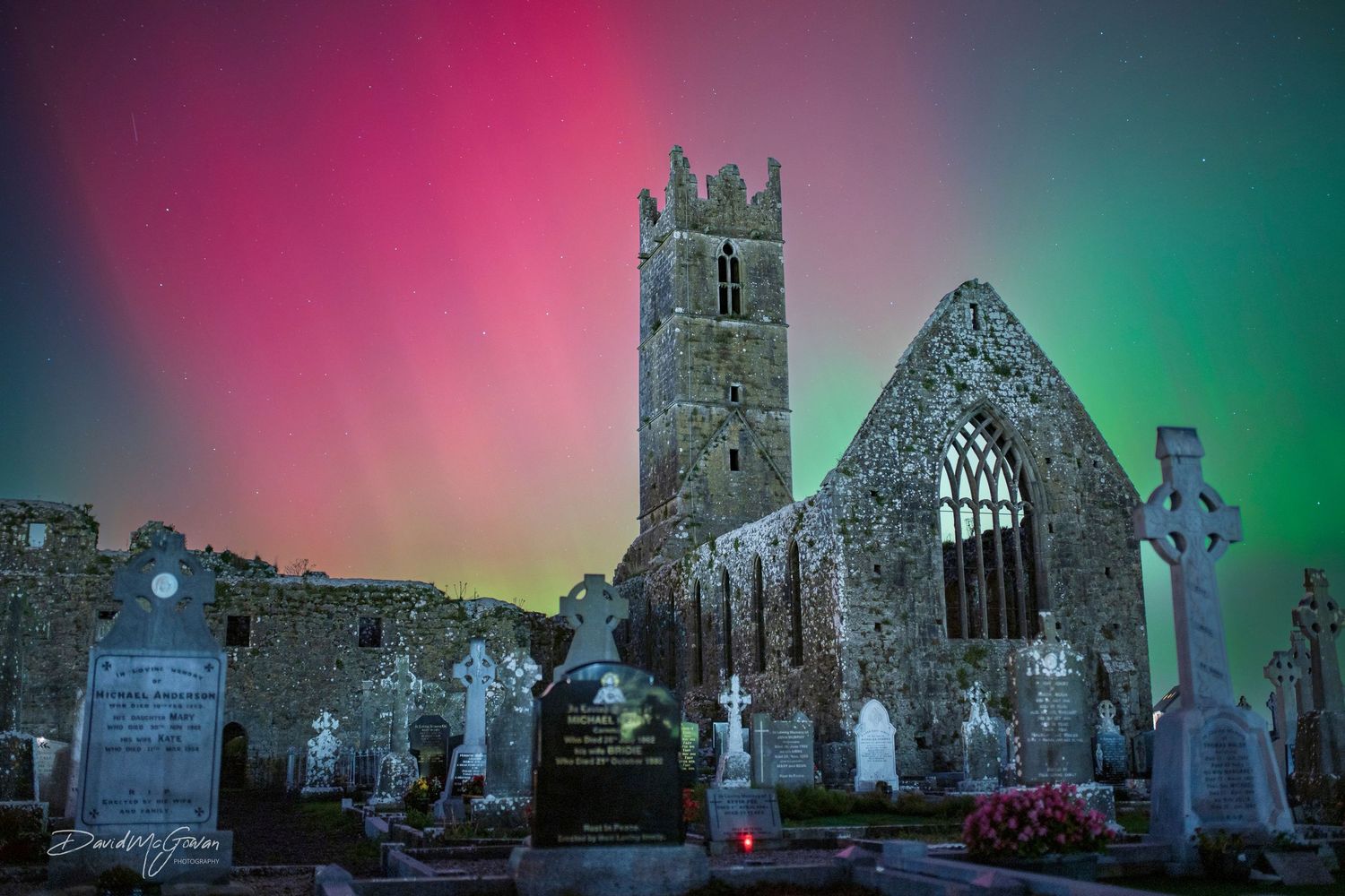 Ancient Irish church ruins with Celtic crosses under a vivid aurora borealis night sky.