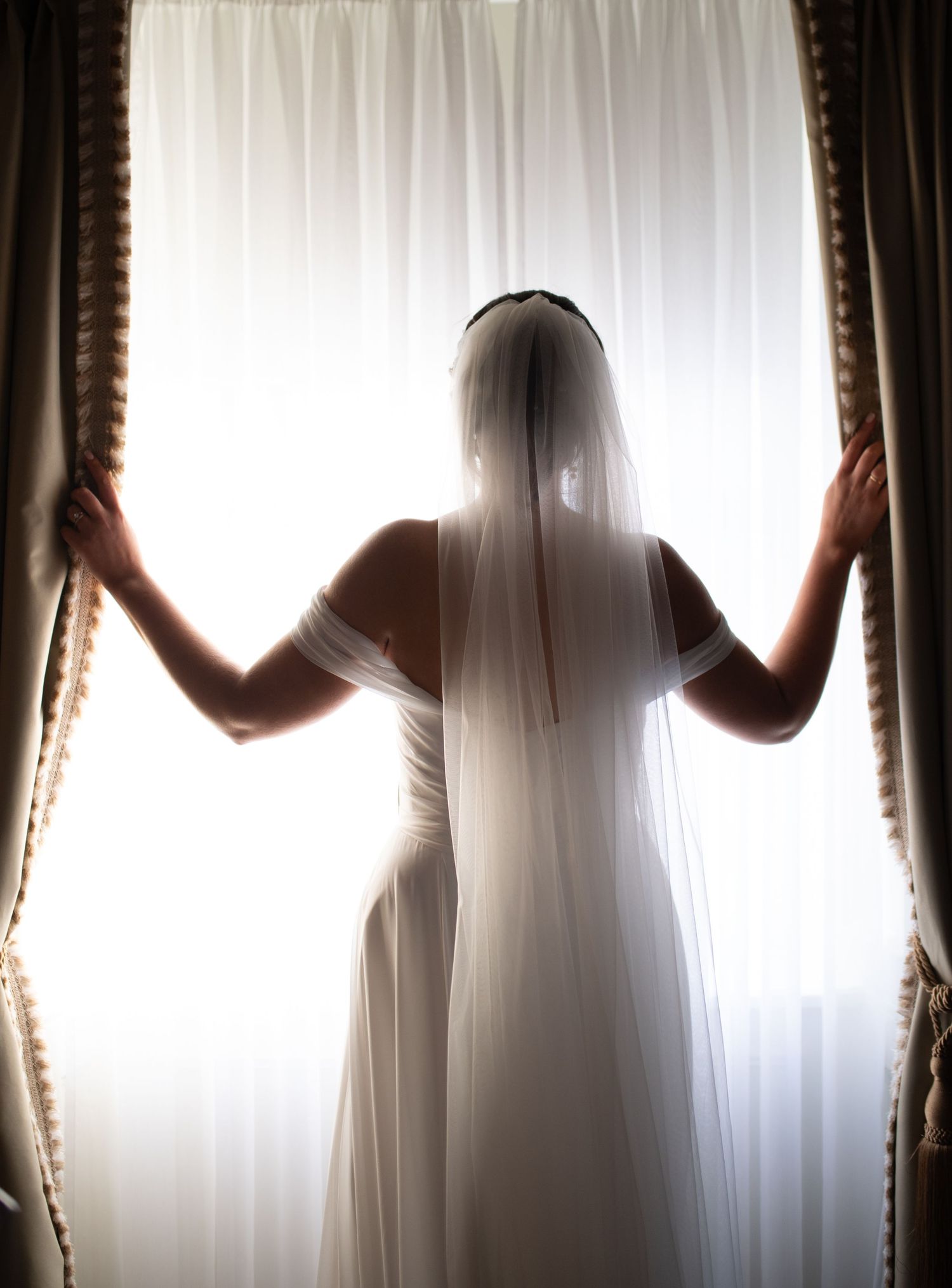 Silhouette of a bride against white curtains creating an ethereal effect.