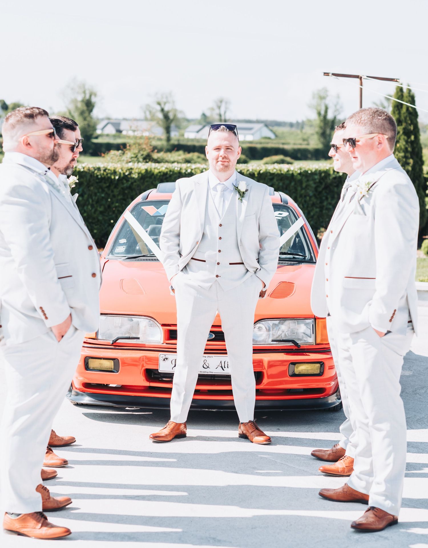 Multiple shots of people in white suits standing in front of a red sports car.