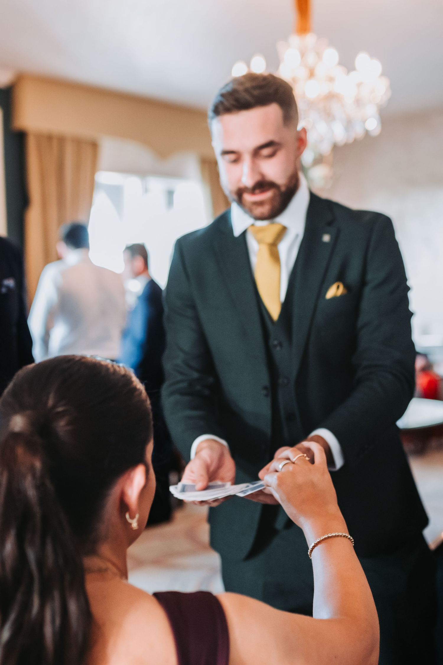 Smiling man in black suit with yellow tie handing documents to a woman at an elegant indoor event.