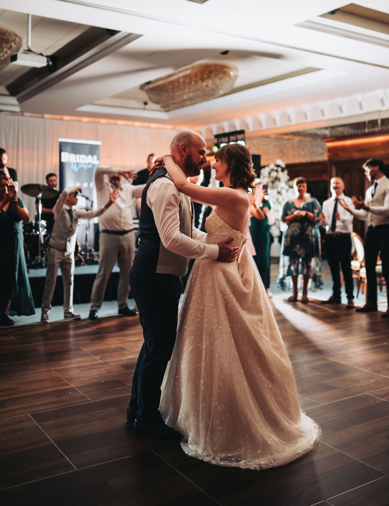 Couples dancing at a wedding reception on a wooden floor with festive lighting.