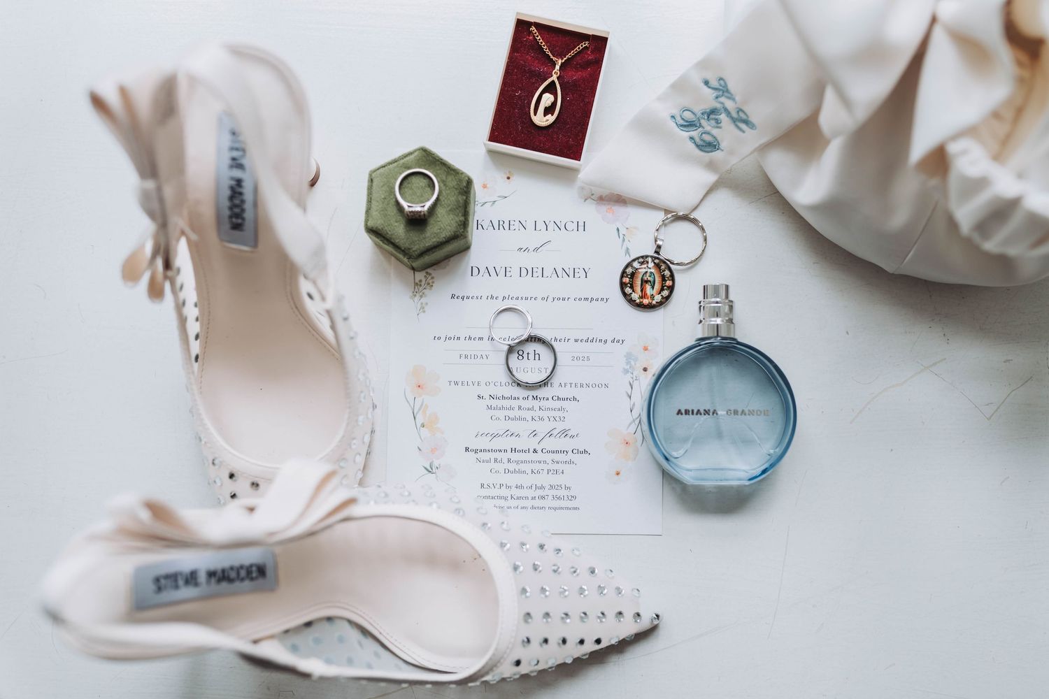 Wedding invitation suite with rings, perfume bottles and delicate accessories styled on light background.