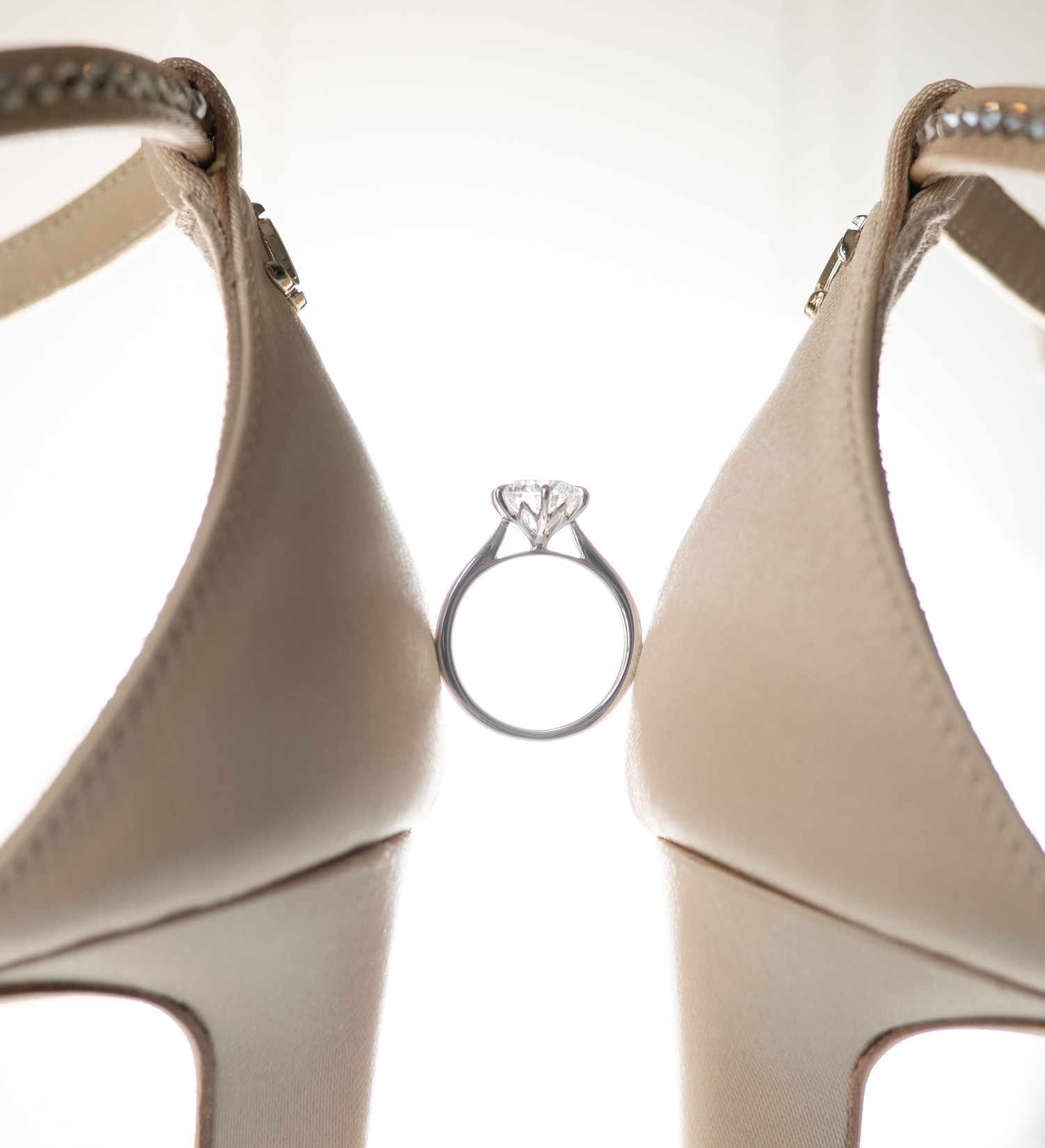 Diamond engagement ring positioned between two elegant cream-colored bridal shoes.