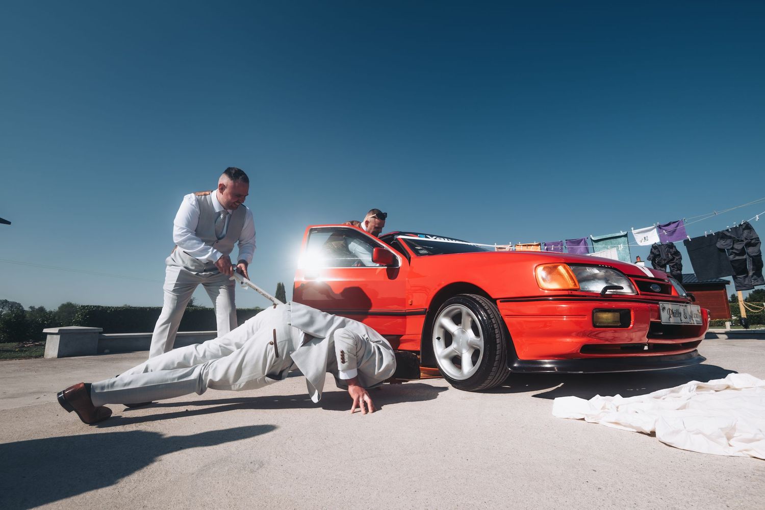 Creative poses with a red sports car on a sunny day wearing all white attire.