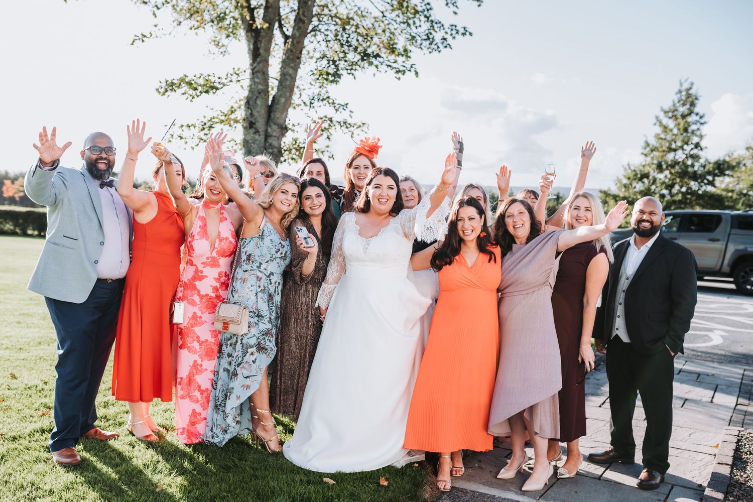Joyful wedding party group photo with bride in white gown surrounded by guests in colorful dresses.
