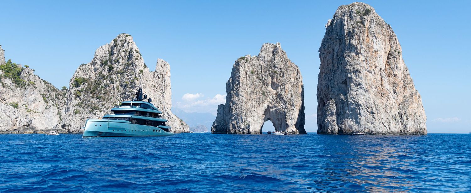 Luxury yacht sailing near the iconic Faraglioni rock formations off the coast of Capri, Italy.