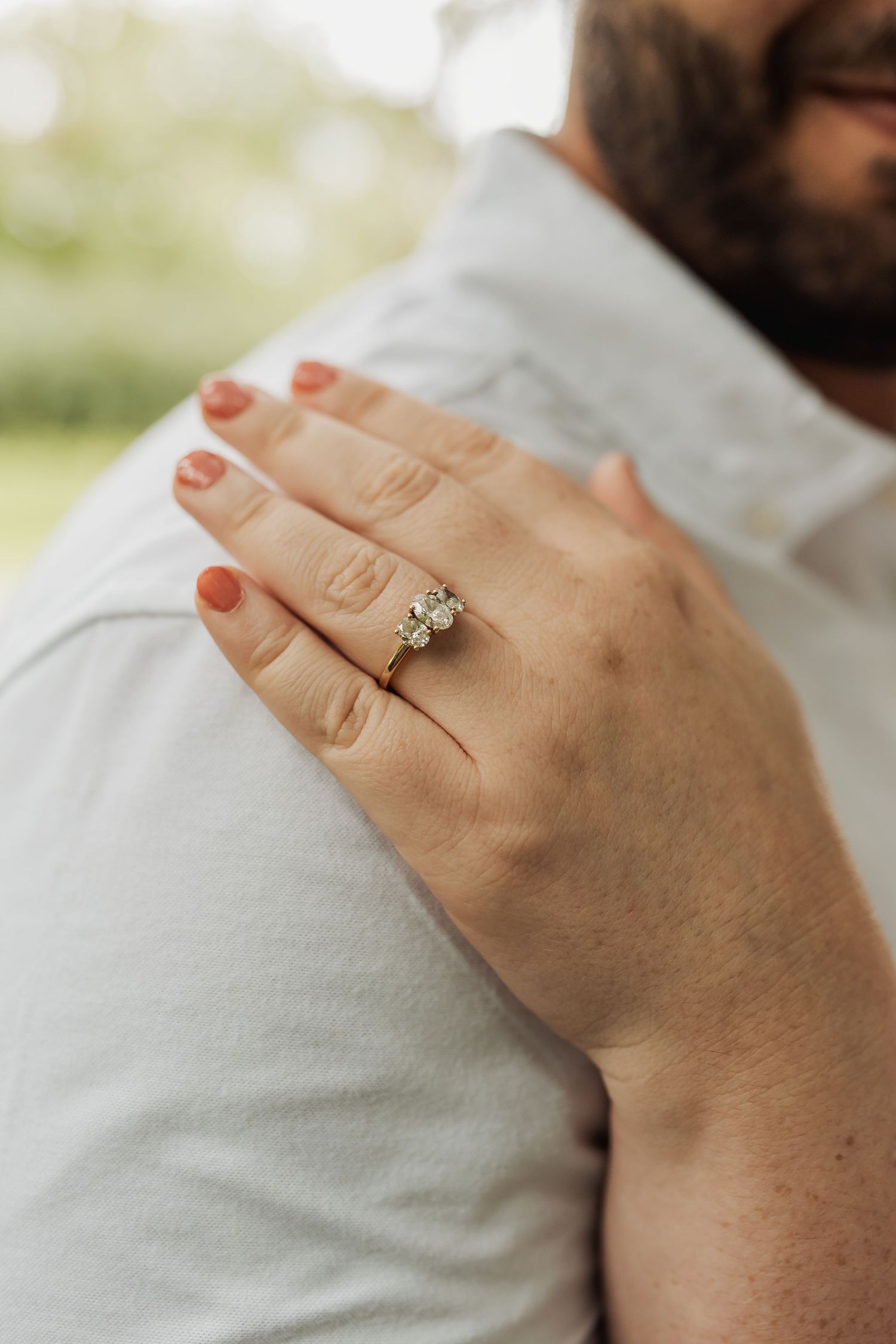 Close-up of a sparkling diamond engagement ring on a woman's hand resting on a man's shoulder.